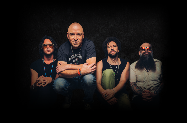 Promotional portrait of American rock band Live, featuring lead singer Ed Kowalczyk crouching center with band members against a dark background.